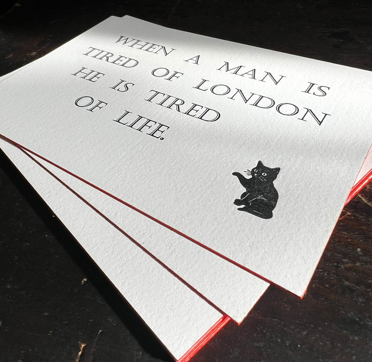 Hand-printed letterpress card reading 'When a man is tired of London he is tired of life', with Buttons the cat and red painted edges
